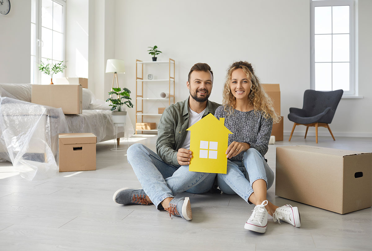 happy couple sitting among boxes on day of moving to their own new home